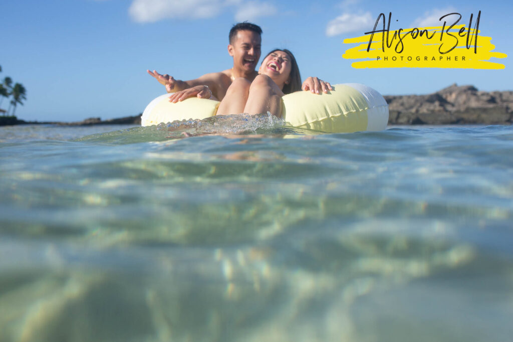 couple playing in water at paradise cove beach, ko olina, oahu by alison bell, photographer