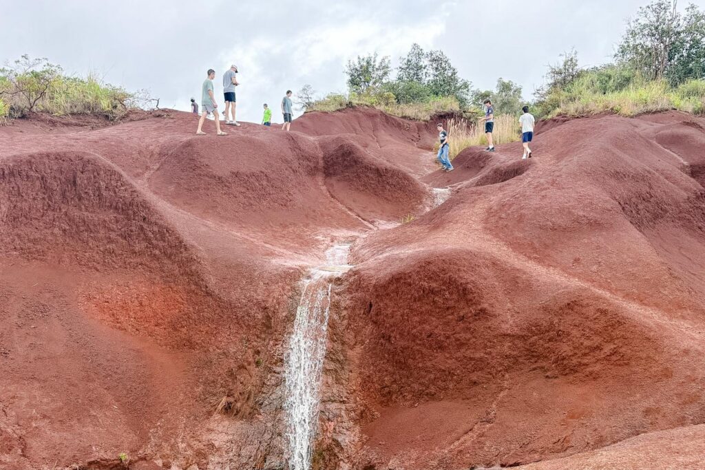 Family exploring a Kauai family hike at a red dirt waterfall in Kauaʻi, Hawaii. Family photos by Alison Bell, photographer in Hawaii.
