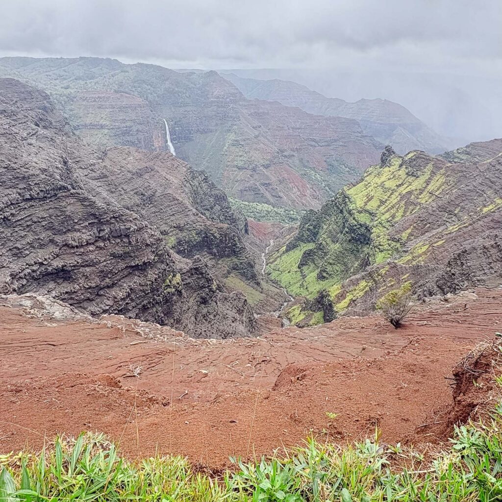 Waimea Canyon overlook with lush green cliffs and waterfall in Kauaʻi, Hawaii. Photography by Alison Bell, photographer in Hawaii.