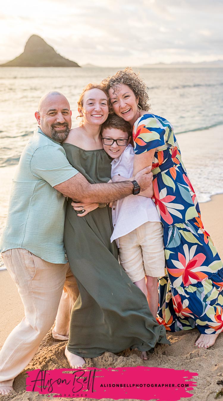 Family hugging together on the beach at Kualoa Regional Park with the Chinaman's Hat. Photography by Alison Bell, photographer in Hawaii.
