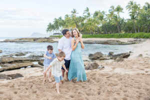 Family walking and playing together on a sandy beach with rocky tide pools and palm trees at Ko Olina in Oʻahu, Hawaii. Photography by Alison Bell, photographer in Hawaii.