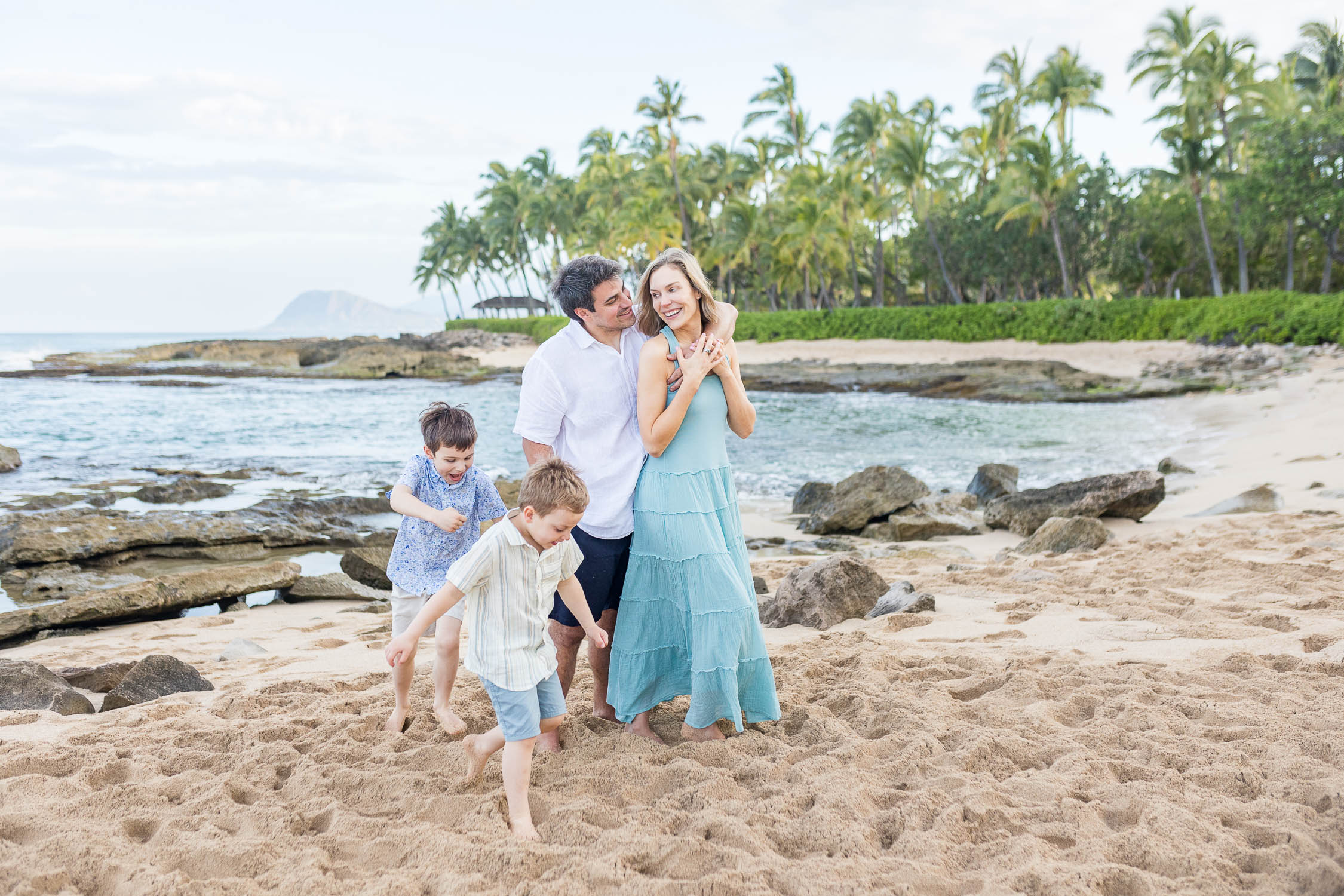 Family walking and playing together on a sandy beach with rocky tide pools and palm trees at Ko Olina in Oʻahu, Hawaii. Photography by Alison Bell, photographer in Hawaii.
